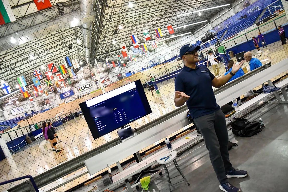 The VeloIQ live board on a screen at the VELO Sports Center infield, with a VeloIQ team member beside it.